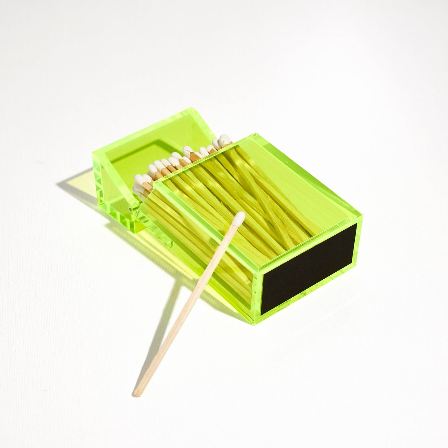 Opened Match holder shaped like a Cigarette Case. Made with neon green acrylic. Case holds White matches in it. Laying flat to feature the striker at the bottom.