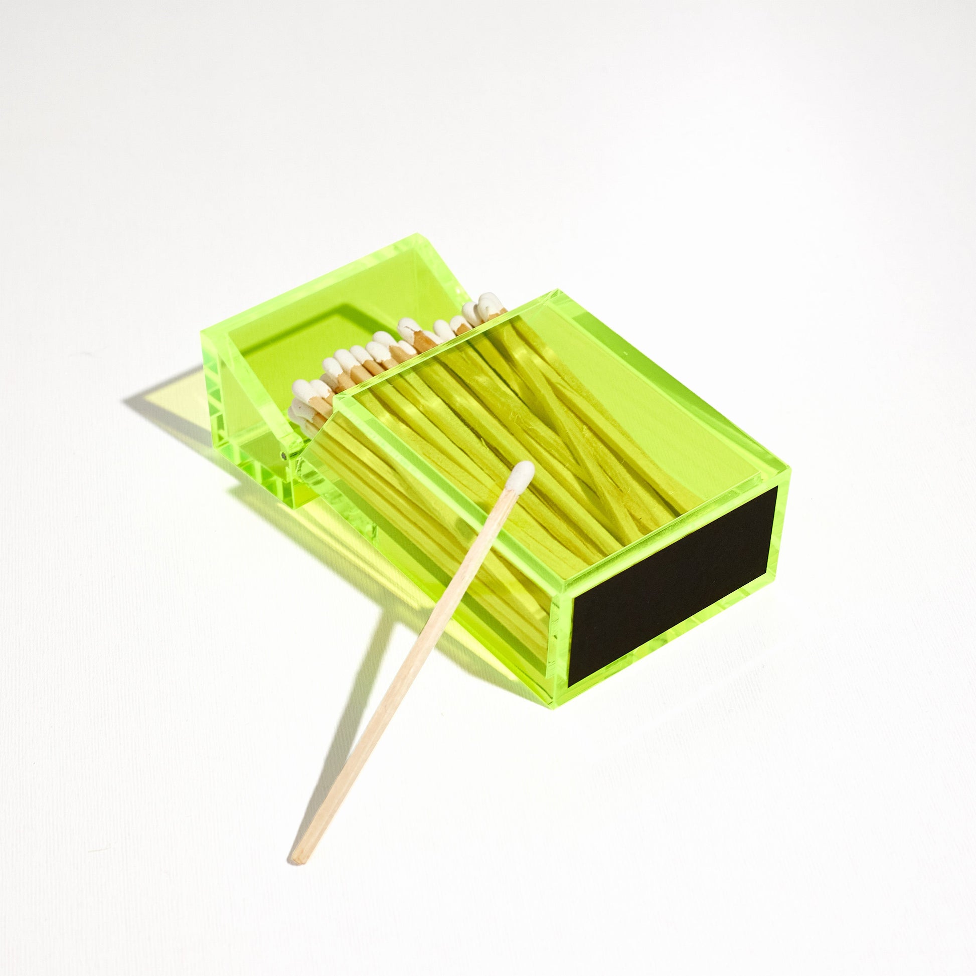 Opened Match holder shaped like a Cigarette Case. Made with neon green acrylic. Case holds White matches in it. Laying flat to feature the striker at the bottom. 