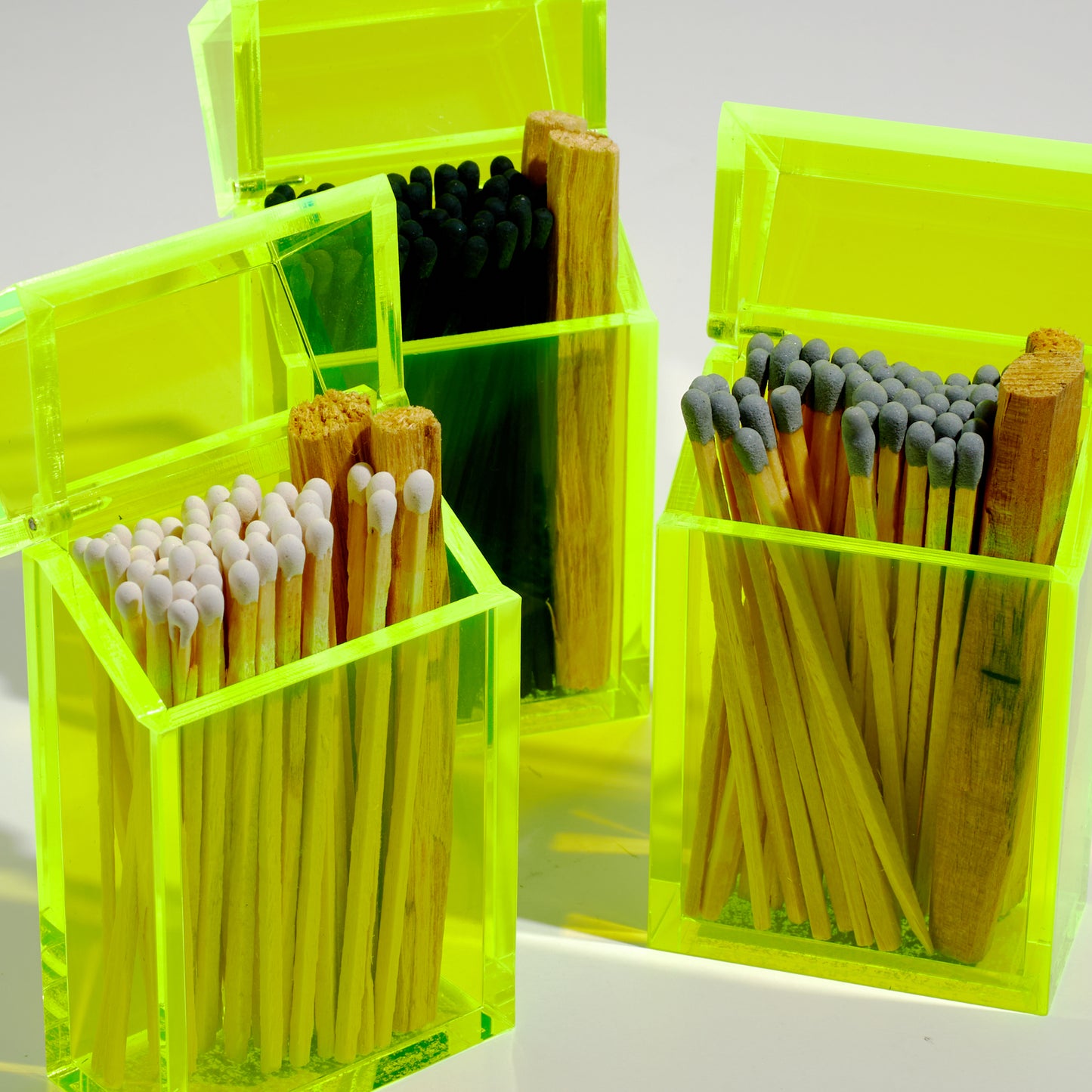 A group of cigarette style neon acrylic cases featuring a variety of match colors such as white, black and gray. In each case there are 2 palo santo sticks.